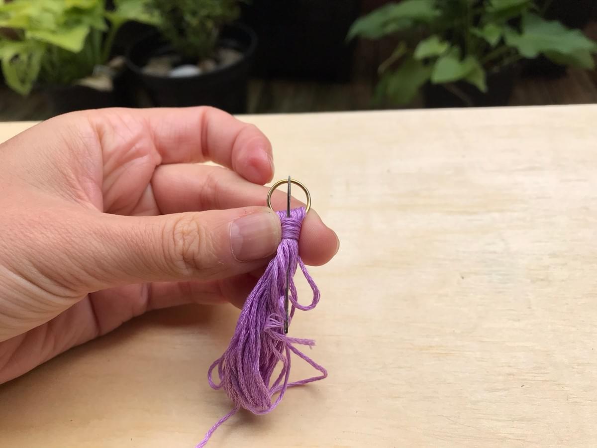 Hand holding the hoop, showing a needle being pushed through the part just wrapped Hand holding the hoop, showing a needle being pushed through the part just wrapped