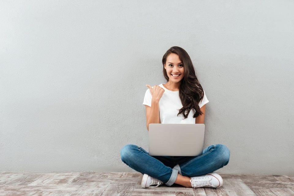 woman sat cross-legged against a wall with laptop give thumbs up woman sat cross-legged against a wall with laptop give thumbs up