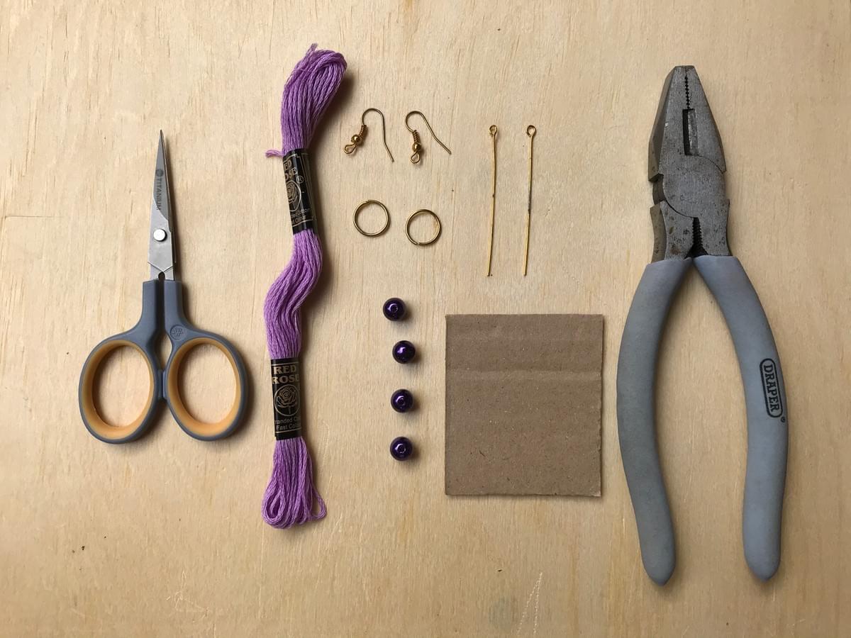 Flat lay of items needed: scissors, embroidery thread, beads, earring hooks, rings, wire, cardboard, pliers Flat lay of items needed: scissors, embroidery thread, beads, earring hooks, rings, wire, cardboard, pliers