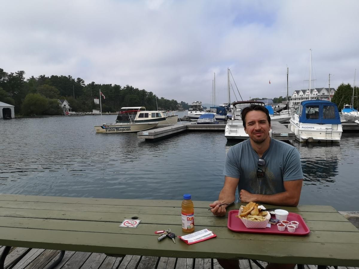 man sitting at a picnic table on a dock eating fish and chips at Herbert fish and chips in Killarney man sitting at a picnic table on a dock eating fish and chips at Herbert fish and chips in Killarney