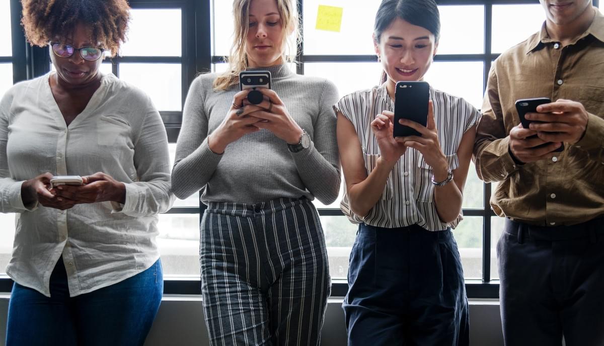 4 people in an office looking captivated by their smartphones 4 people in an office looking captivated by their smartphones