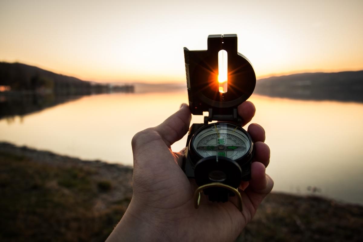 A hand holding a compass looking out over water A hand holding a compass looking out over water