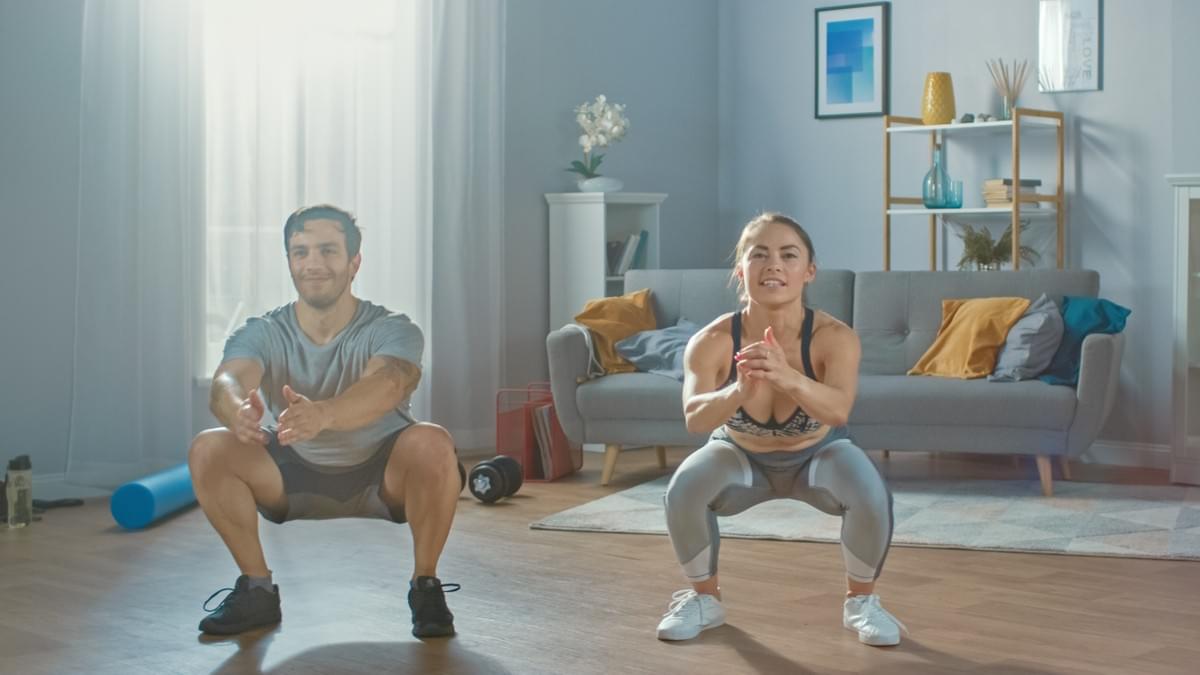 Un homme et une femme en tenue de sport, faisant des squats dans leur salon. Fitness, sport, maison, confinement, en ligne, pandémie, coronavirus, couple, santé, intérieur, adaptation, bien-être Un homme et une femme en tenue de sport, faisant des squats dans leur salon. Fitness, sport, maison, confinement, en ligne, pandémie, coronavirus, couple, santé, intérieur, adaptation, bien-être