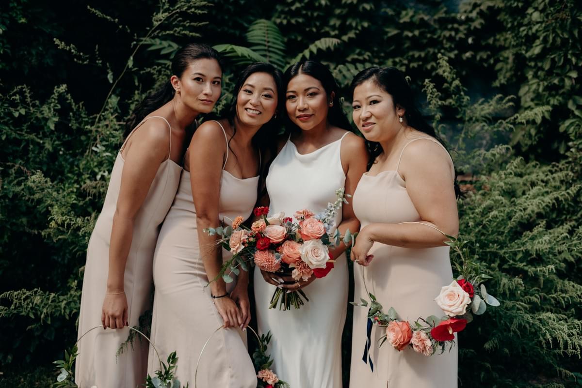 Bride holding a lush bridal bouquet poses with her bridesmaids who are holding hoop bouquets. Bride holding a lush bridal bouquet poses with her bridesmaids who are holding hoop bouquets.