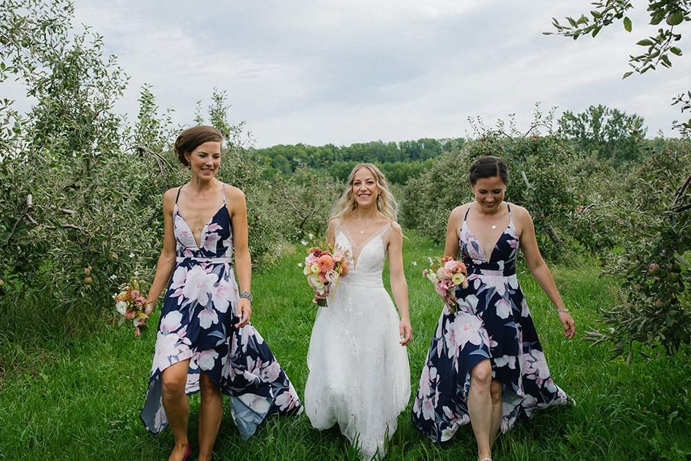 Wedding party walks through apple orchard with bouquets made with locally-grown flowers Wedding party walks through apple orchard with bouquets made with locally-grown flowers
