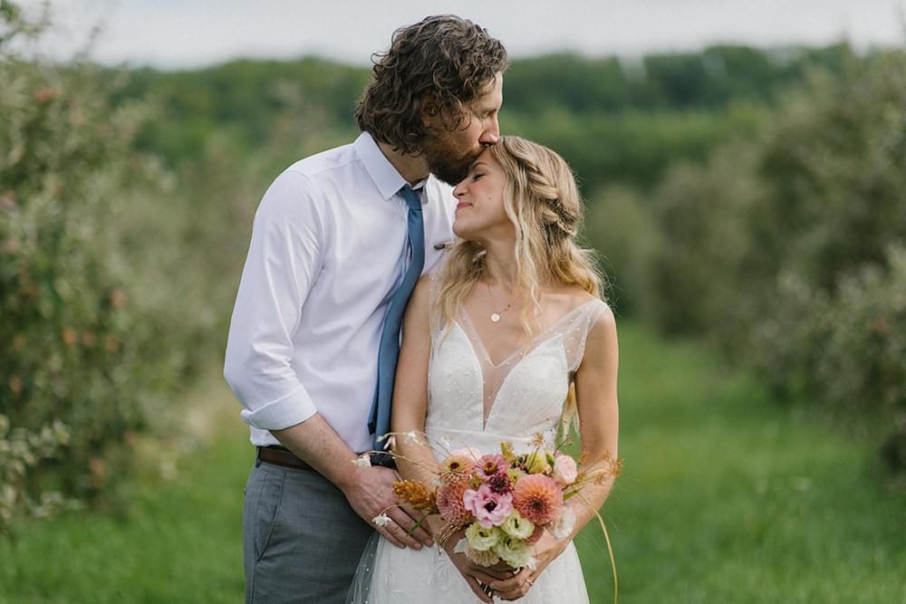 Groom kisses bride's forehead after romantic wedding ceremony at an apple orchard Groom kisses bride's forehead after romantic wedding ceremony at an apple orchard