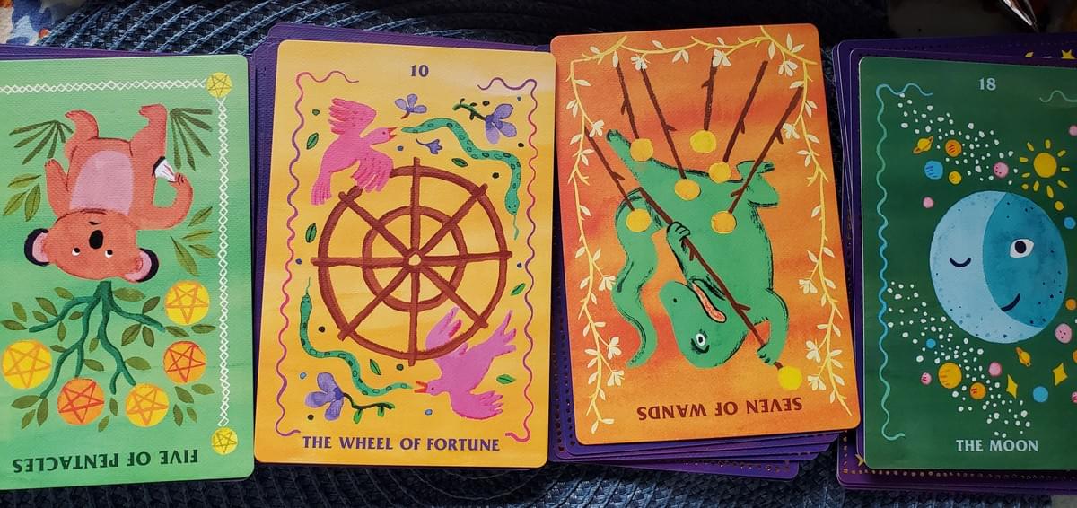 4 Tarot Cards courtesy of The Affirmators! Tarot ©2019 Suzi Barrett Five of Pentacles - An upside down card with Koala holding and empty pocket uner a tree where the fruits are pentacles. The Wheel of Fortune - A wooden spoked wheel with a bird and snake chasing each other around at mirror opposites. Seven of Wands - An upside down card depicting an alligaor battle seven wands. The Moon - A full moon winking against a galaxy. 4 Tarot Cards courtesy of The Affirmators! Tarot ©2019 Suzi Barrett Five of Pentacles - An upside down card with Koala holding and empty pocket uner a tree where the fruits are pentacles. The Wheel of Fortune - A wooden spoked wheel with a bird and snake chasing each other around at mirror opposites. Seven of Wands - An upside down card depicting an alligaor battle seven wands. The Moon - A full moon winking against a galaxy.