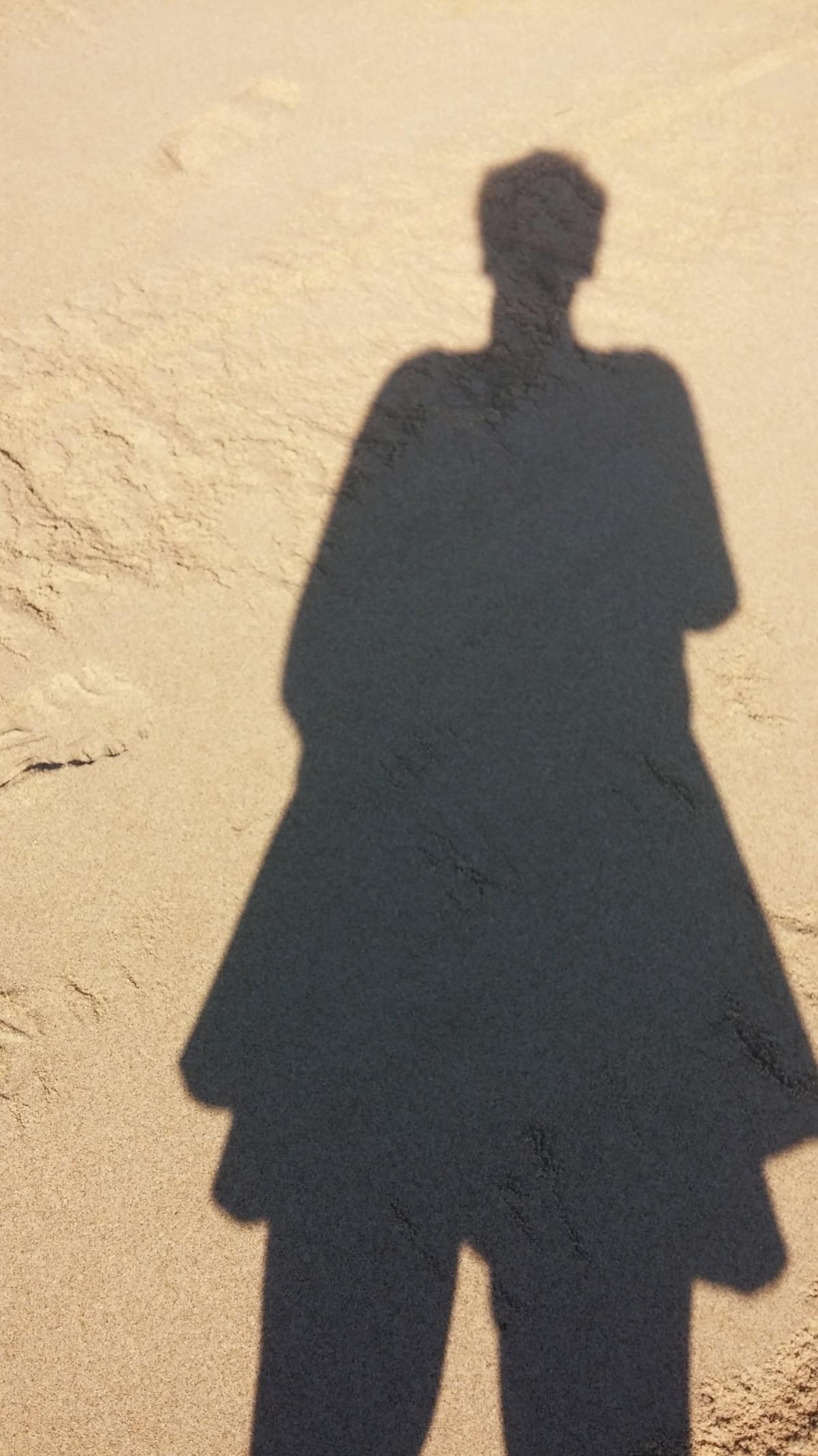 A shadow of a person on the sand from head to knee. They are elongated and roughly triangular. A shadow of a person on the sand from head to knee. They are elongated and roughly triangular.