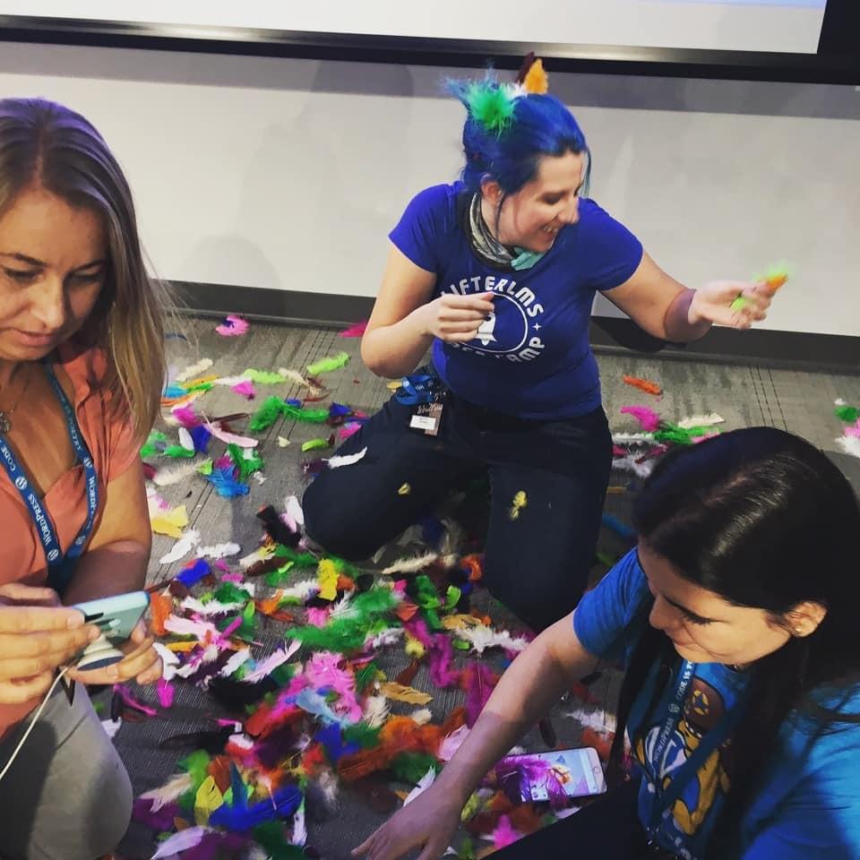 Kitty and friends kneeling on the floor in a pile of colorful feathers after a speaking engagement Kitty and friends kneeling on the floor in a pile of colorful feathers after a speaking engagement