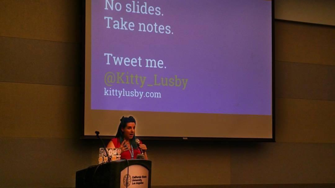 Kitty speaking at an event with a slide that says No Slides, Take Notes, Tweet Me Kitty speaking at an event with a slide that says No Slides, Take Notes, Tweet Me