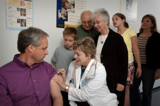 A man receiving a vaccine while a multigenerational family watches A man receiving a vaccine while a multigenerational family watches