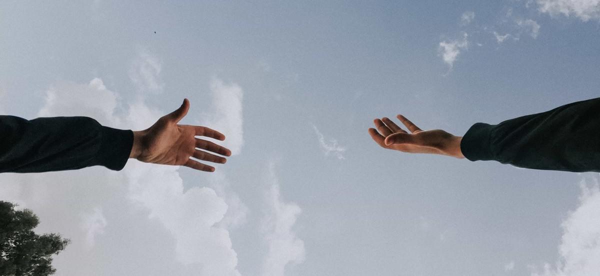 Shot from below, a picture of hands reaching towards each other with the backdrop of a partly cloudy daytime sky Shot from below, a picture of hands reaching towards each other with the backdrop of a partly cloudy daytime sky