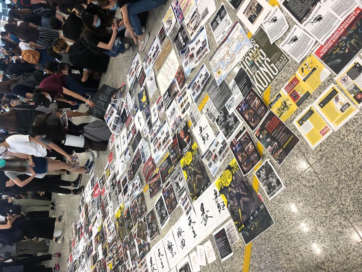 抗議民眾克難的把文宣品擺在地上,吸引來往旅客注意。(圖片來源:作者提供) 抗議民眾克難的把文宣品擺在地上,吸引來往旅客注意。(圖片來源:作者提供)
