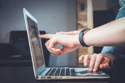 Someone useing a laptop, the photo is taken from the side on. Another personis pointing to something on the screen. Someone useing a laptop, the photo is taken from the side on. Another personis pointing to something on the screen.