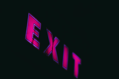 A black background with a pink neon sign across that reads: Exit. A black background with a pink neon sign across that reads: Exit.