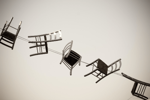 Five chairs running diaganally in a row from top left to bottom right. The chairs are hung up on wires. Five chairs running diaganally in a row from top left to bottom right. The chairs are hung up on wires.