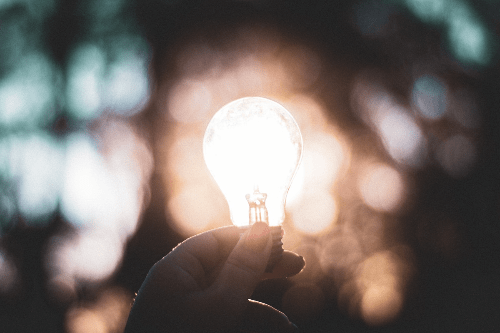 a hand holding a lightbulb which is light from the sun shining behind it. a hand holding a lightbulb which is light from the sun shining behind it.