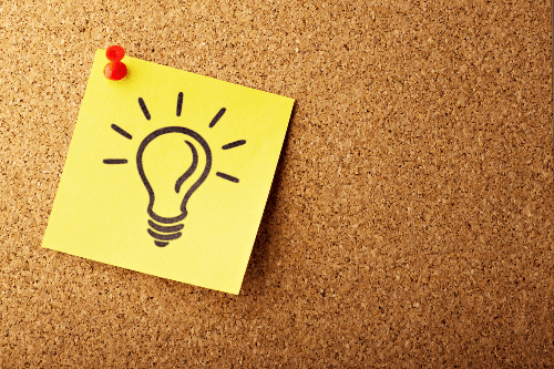 A closeup of a cork board with a singal yellow postet note pinned on with a red pin. The postitmote has a light lightbulb drawn on it. A closeup of a cork board with a singal yellow postet note pinned on with a red pin. The postitmote has a light lightbulb drawn on it.