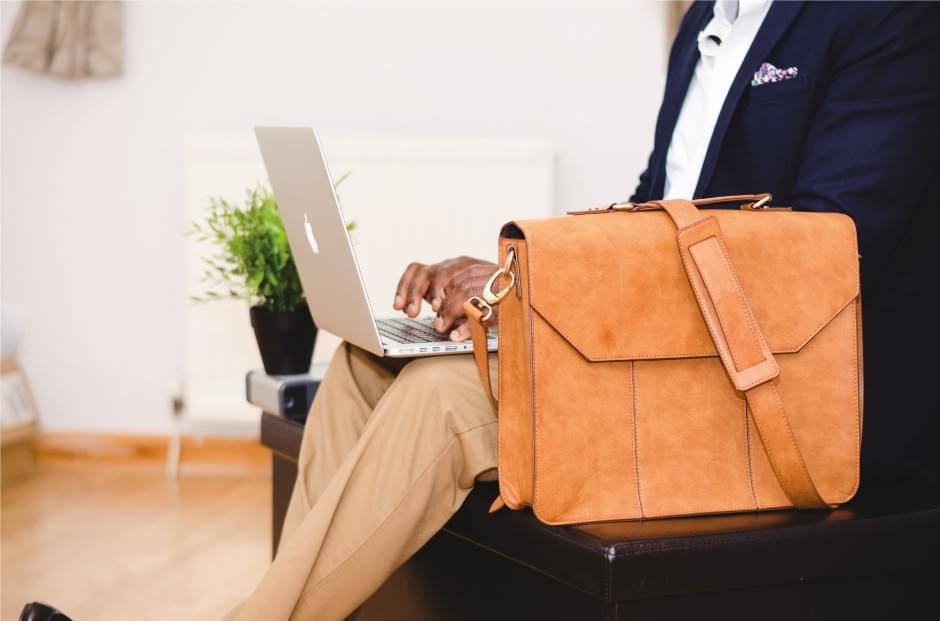A man typing on a macbook, next to a leather briefcase A man typing on a macbook, next to a leather briefcase