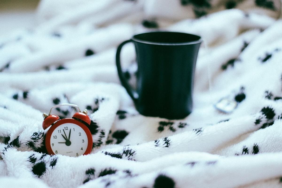 A photo of a coffee cup and an alarm clock on a blanket on a bed as featured in The Purple Dog Blog post "* Simple Rules for Better Mornings" by The Purple Dog Vegan A photo of a coffee cup and an alarm clock on a blanket on a bed as featured in The Purple Dog Blog post "* Simple Rules for Better Mornings" by The Purple Dog Vegan