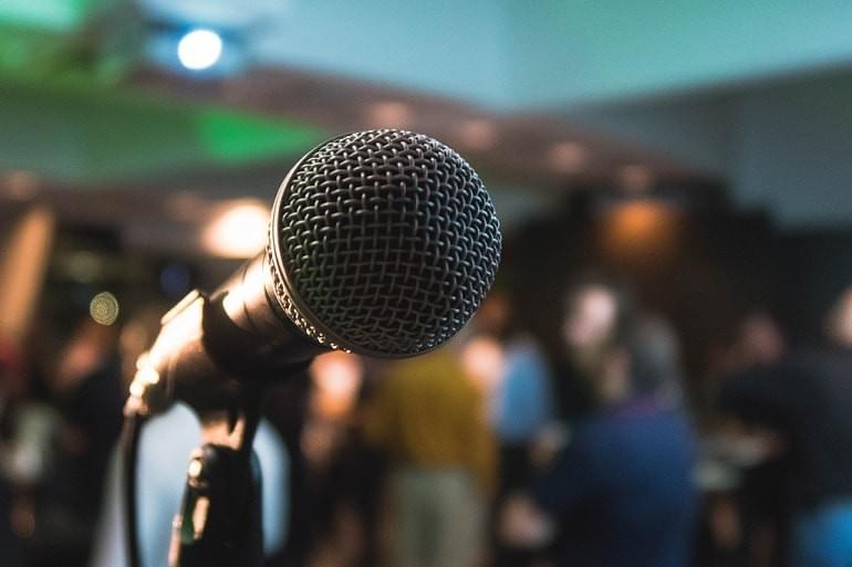 A photo of a microphone in a stand in front of a crowd of people, as featured in the blog post, "You Aren't Like Oog the Caveman" from The Purple Dog Vegan A photo of a microphone in a stand in front of a crowd of people, as featured in the blog post, "You Aren't Like Oog the Caveman" from The Purple Dog Vegan