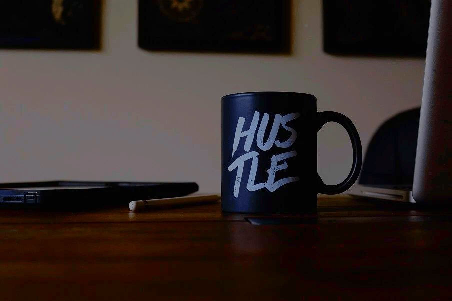 Coffee cup on a desk with the word Hustle written on it- from the "Hustle Culture" blog post from The Purple Dog Vegan Coffee cup on a desk with the word Hustle written on it- from the "Hustle Culture" blog post from The Purple Dog Vegan