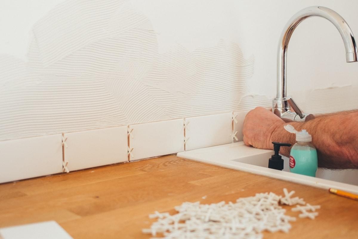 Man tiling the wall above the kitchen work top Man tiling the wall above the kitchen work top