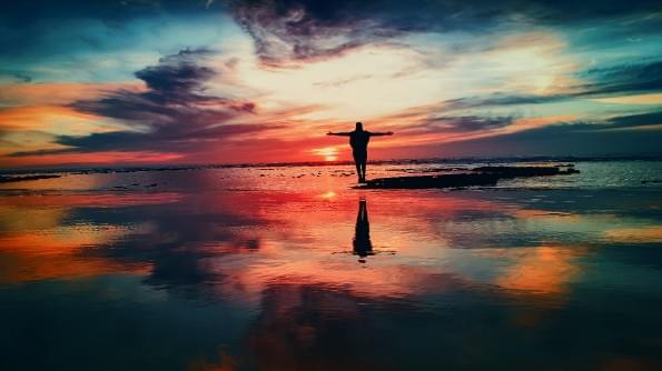 A figure with arms outstretched, stands on a seashore in homage to the sun. A figure with arms outstretched, stands on a seashore in homage to the sun.