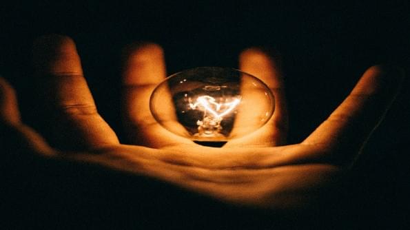 A hand holds a glowing lightbulb. All else is dark. A hand holds a glowing lightbulb. All else is dark.