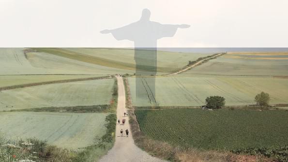 A path leads through meadows. There are people walking the path. The figure of Christ rises high above the meadow. A path leads through meadows. There are people walking the path. The figure of Christ rises high above the meadow.