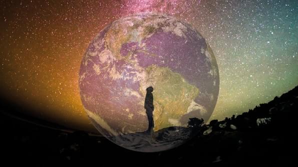 A figure is silhouetted against stars. Behind him is the Earth as seen from space. A figure is silhouetted against stars. Behind him is the Earth as seen from space.