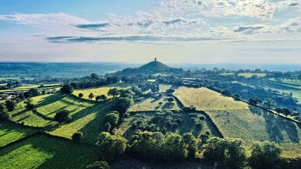 Glastonbury Tor is seen from a distance surrounded by fields and hedgerows. Glastonbury Tor is seen from a distance surrounded by fields and hedgerows.
