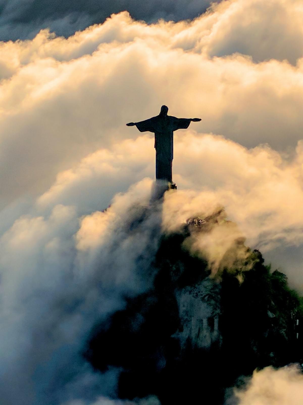 Image of a statue of Christ, arms outstretched, gazing upon the world from a cloud-shrouded mountain top. Image of a statue of Christ, arms outstretched, gazing upon the world from a cloud-shrouded mountain top.