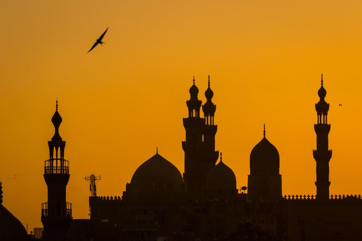 Image of minarets and domes of an eastern mosque silhouetted against a bright sunset sky. Image of minarets and domes of an eastern mosque silhouetted against a bright sunset sky.