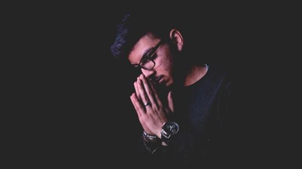 A man, head bowed, and hands held in prayer, is silhouetted against a black background. A man, head bowed, and hands held in prayer, is silhouetted against a black background.