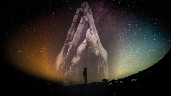 A figure stand silhouetted against a starlit sky. All but filling the sky are hands clasped in prayer. A figure stand silhouetted against a starlit sky. All but filling the sky are hands clasped in prayer.