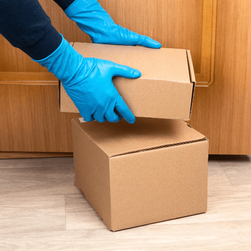 A gloved delivery-person puts a box down in front of a door. A gloved delivery-person puts a box down in front of a door.