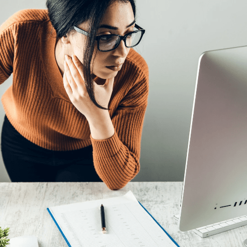 A woman in an orange top peers at a large computer desktop as she readies herself to learn. A woman in an orange top peers at a large computer desktop as she readies herself to learn.