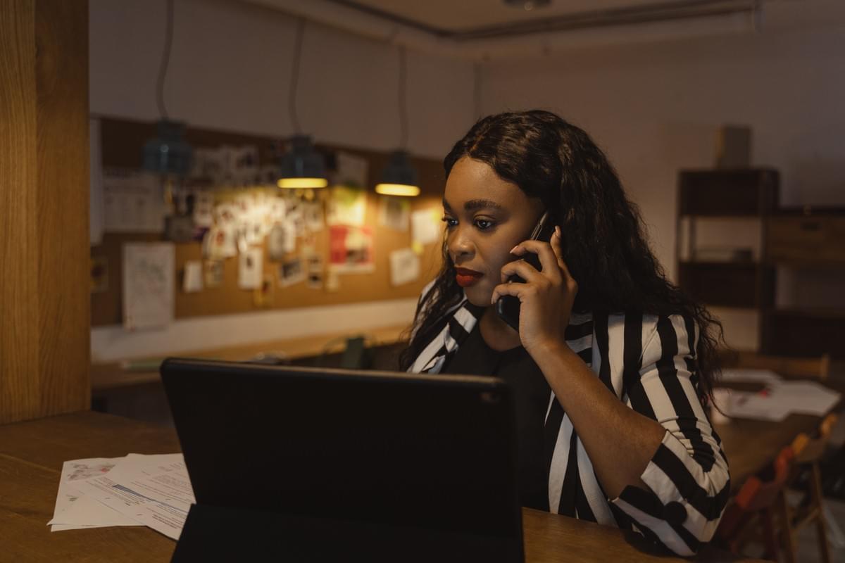 Black woman works at home on her computer while she speaks on the phone. Black woman works at home on her computer while she speaks on the phone.