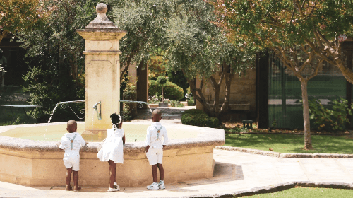 Three young children in white stand before a European fountain. Three young children in white stand before a European fountain.