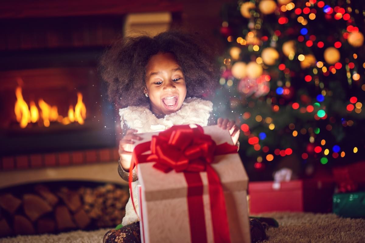 a young girl excitedly opening her present in front of a christmas tree a young girl excitedly opening her present in front of a christmas tree