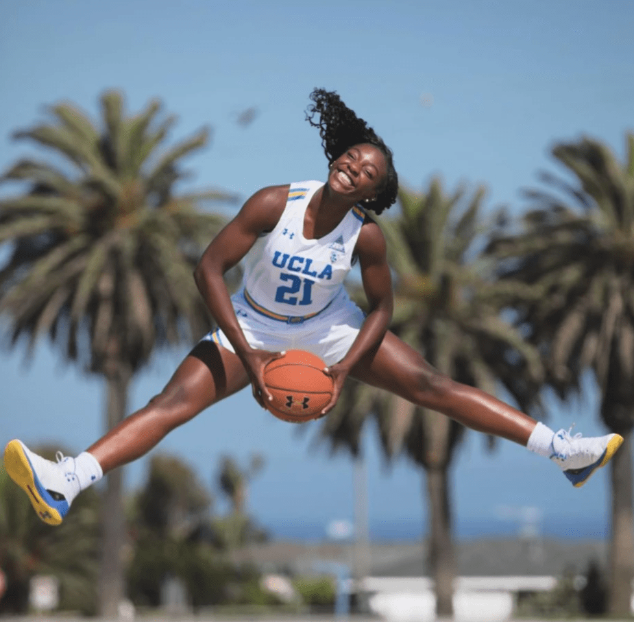 Michaela jumps smiling in the splits holding basketball and wearing UCLA jersey. Palm trees in the background. Michaela jumps smiling in the splits holding basketball and wearing UCLA jersey. Palm trees in the background.