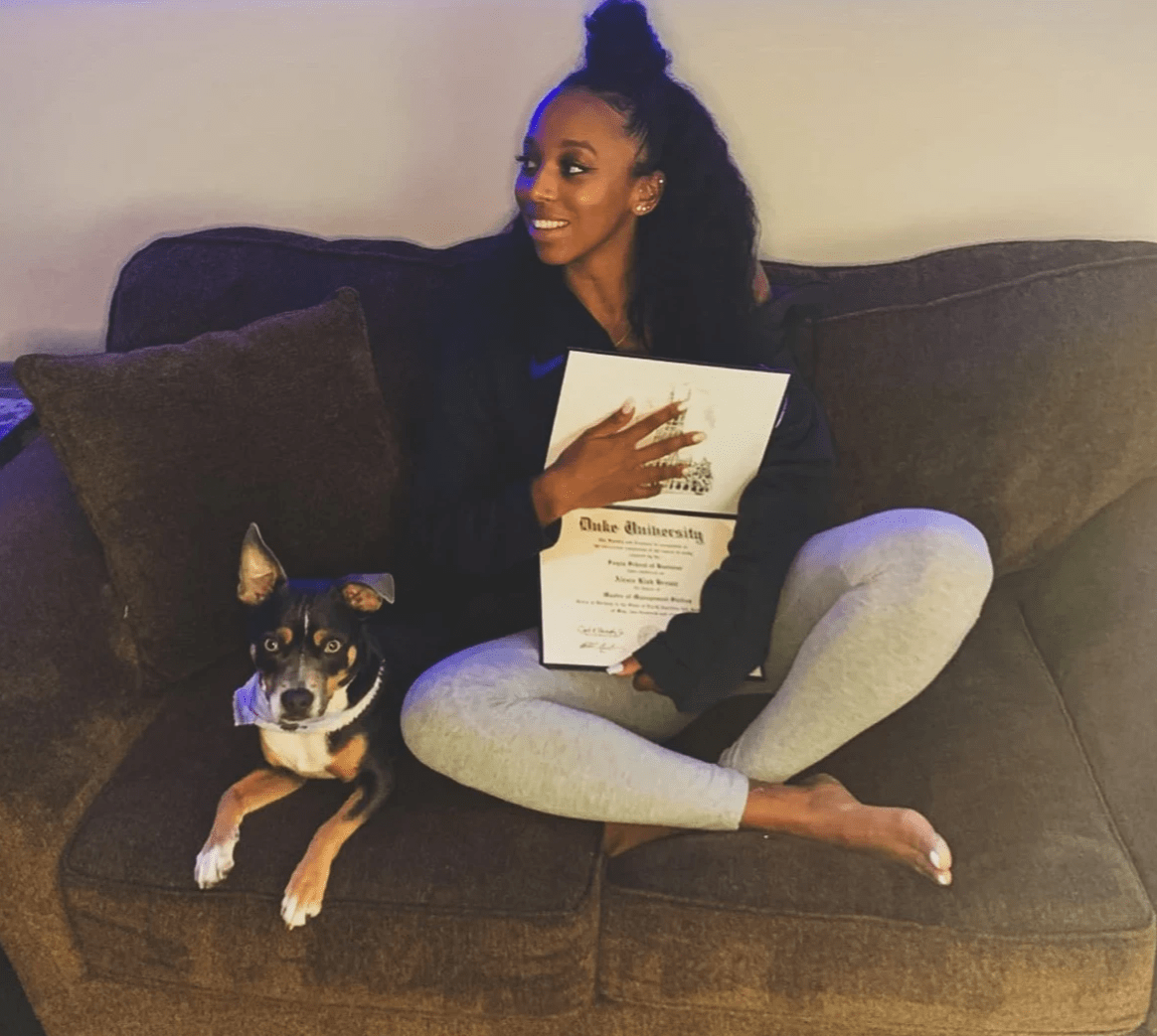 Lexie Brown sits on couch holding Duke University diploma with black and brown dog sitting next to her. Lexie Brown sits on couch holding Duke University diploma with black and brown dog sitting next to her.