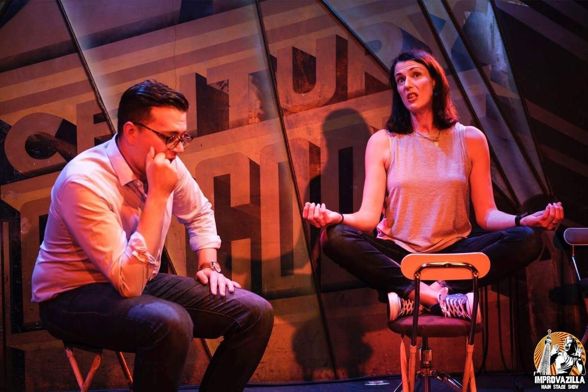 Christiane (right) with another improvisor on stage. She is sitting on a chair in the lotus position while the other improvisor listens attentively. Christiane (right) with another improvisor on stage. She is sitting on a chair in the lotus position while the other improvisor listens attentively.
