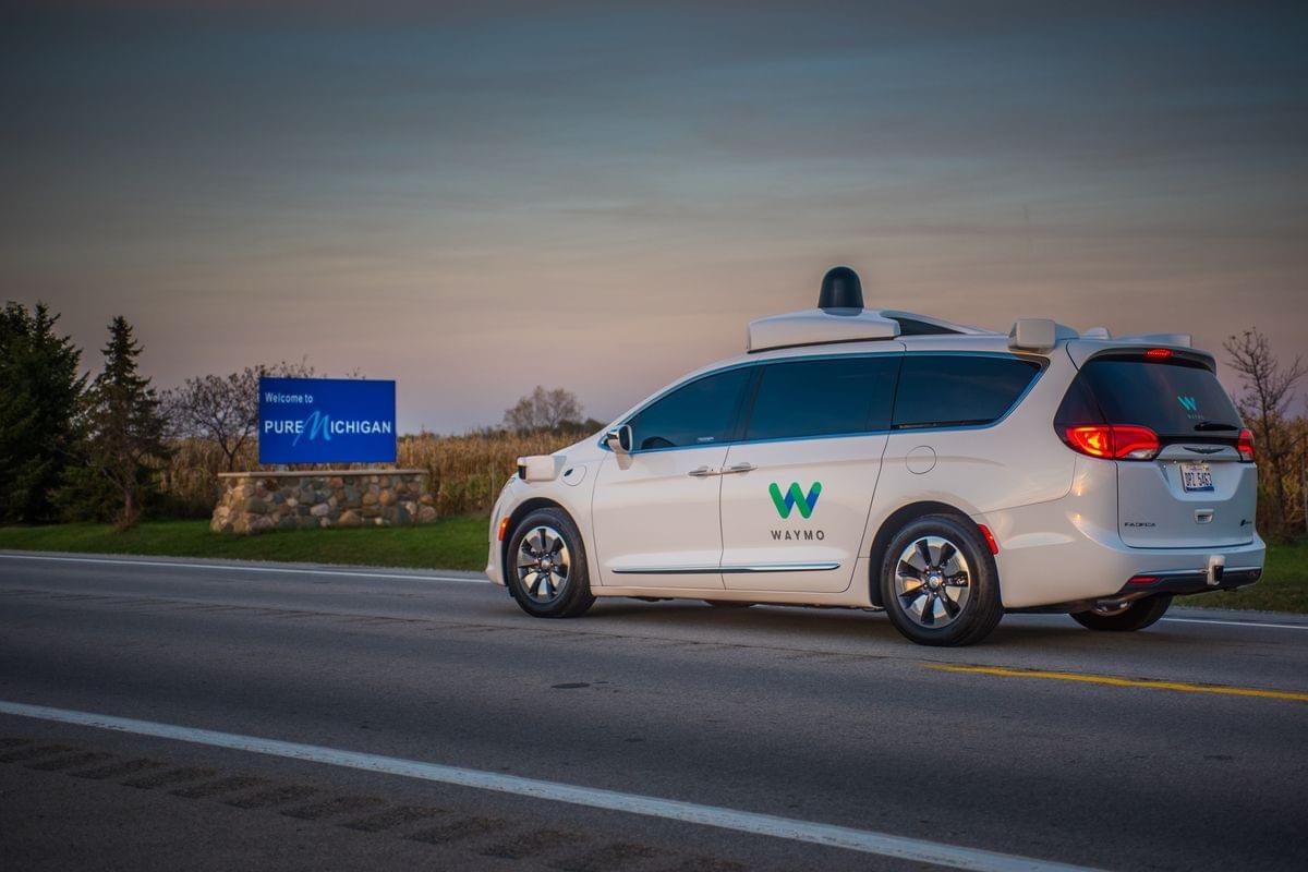 Photograph of a Waymo self-driving van on the road with a Pure Michigan sign in the background. Photograph of a Waymo self-driving van on the road with a Pure Michigan sign in the background.