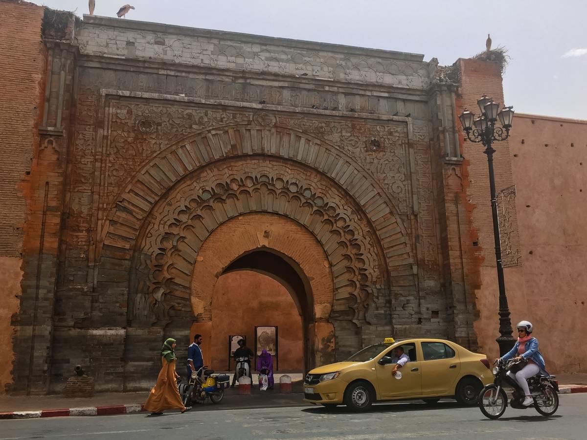 A woman wearing a hijab walking, a yellow taxi and motorbike passing an open gate in marrakech. A woman wearing a hijab walking, a yellow taxi and motorbike passing an open gate in marrakech.