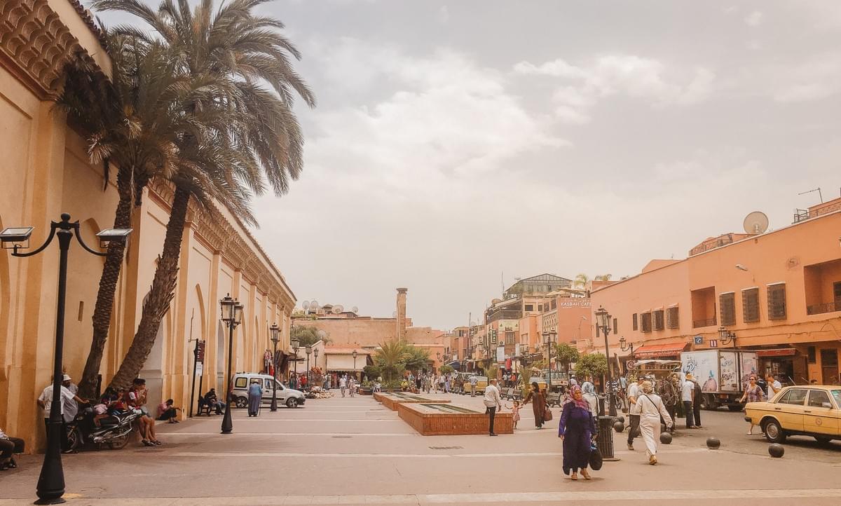 Busy medina Street near El Mouassine Mosque, palm trees, light posts, people, woman in hijab and yellow taxi Busy medina Street near El Mouassine Mosque, palm trees, light posts, people, woman in hijab and yellow taxi