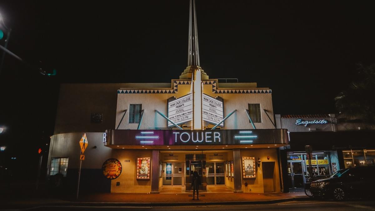 Tower Theater in Miami at night with neon lights and marquee and girl standing alone Tower Theater in Miami at night with neon lights and marquee and girl standing alone