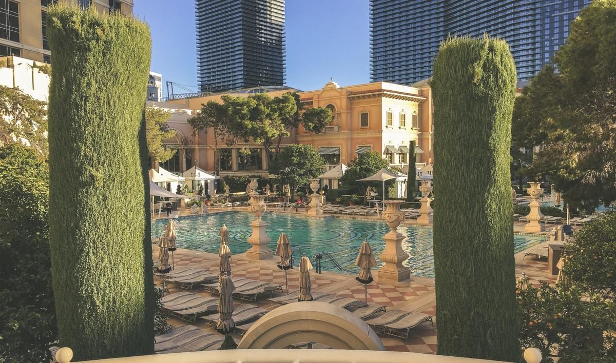 A view of the Bellagio pool hotel facade with plants, trees, lounge chairs, umbrella, cabanas, in the winter A view of the Bellagio pool hotel facade with plants, trees, lounge chairs, umbrella, cabanas, in the winter