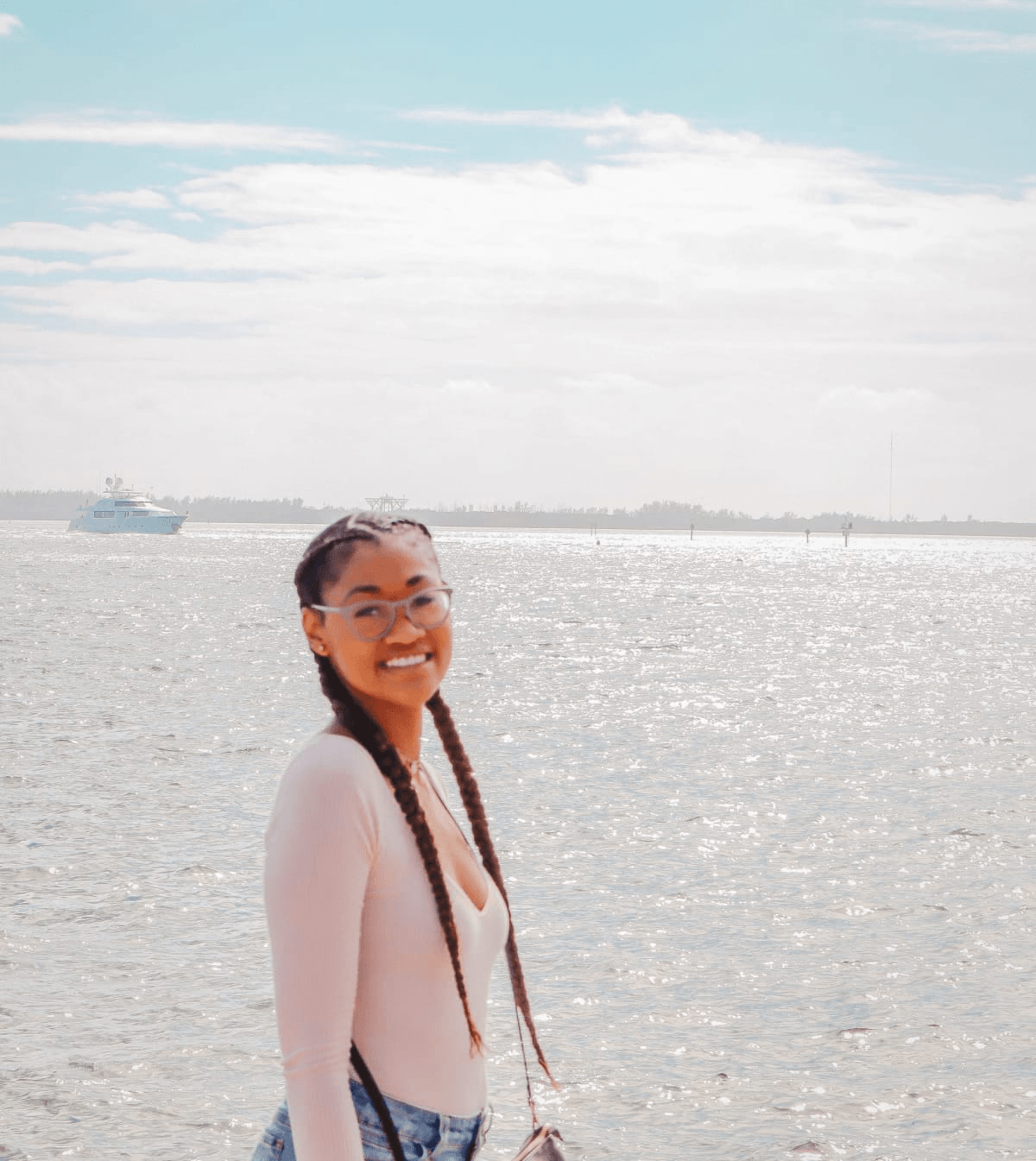 Black girl with french braids smiling by the ocean with boat in the background Black girl with french braids smiling by the ocean with boat in the background